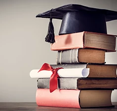 stack of books with a graduation cap (mortarboard) placed on top, and a rolled-up diploma tied with a red ribbon