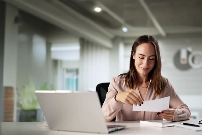 Smiling woman in an office, holding a check letter in her hand