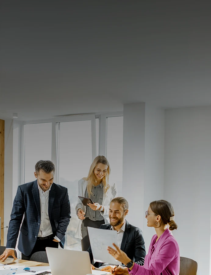 4 pessoas numa sala de reuniões, com computador e portátil, sorridentes