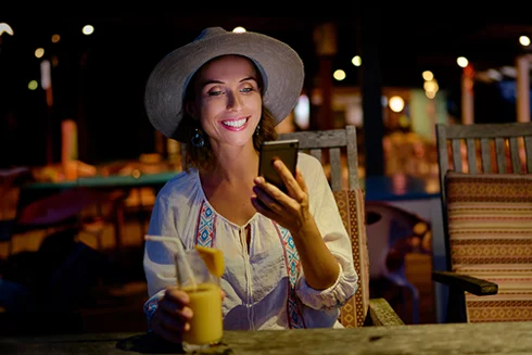 woman sitting at a café table outside, at night, smiling with a phone in her hand