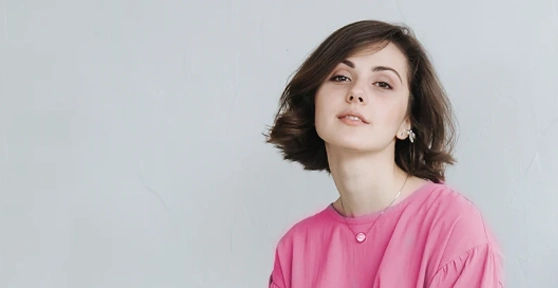 Mulher jovem de cabelo escuro e curto a olhar para a câmara com uma t-shirt rosa