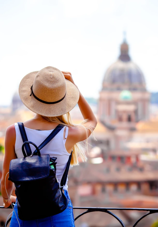 Girl with her back turned, wearing a hat and a backpack, looking at a monument in the distance