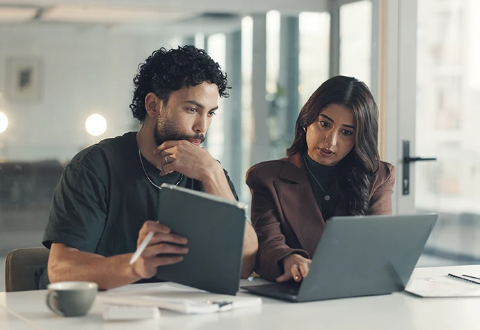 Um homem e uma mulher a analizar dados no ecrâ de um computador