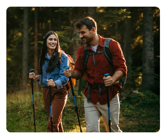 Casal faz caminhada na floresta com mochilas e bastões de trekking