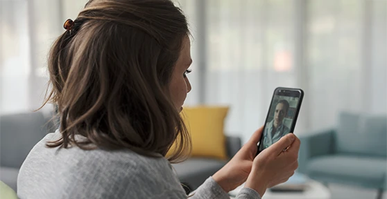mulher sentada em casa, em videochamada no telemóvel com médico