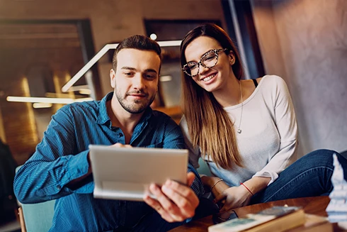 couple sitting on coffee table, holding tablet