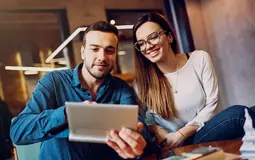 Casal sentado numa mesa de café, a mexer num tablet