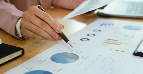 Mão a apontar para um gráfico circular em documentos de análise financeira