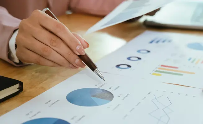 Mão a apontar para um gráfico circular em documentos de análise financeira