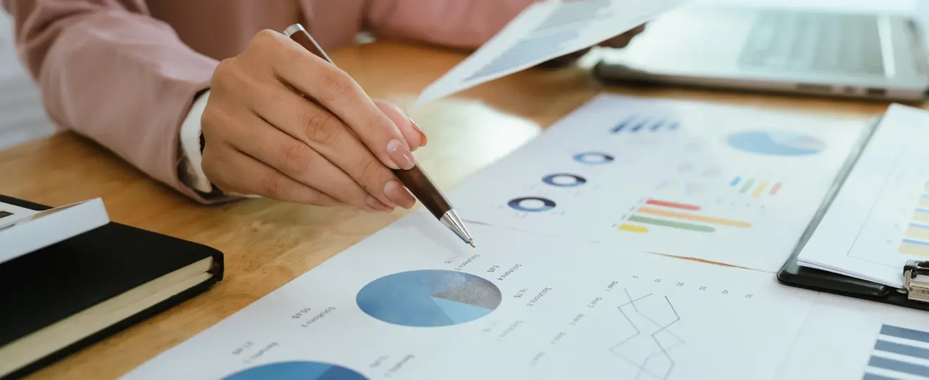 Mão a apontar para um gráfico circular em documentos de análise financeira