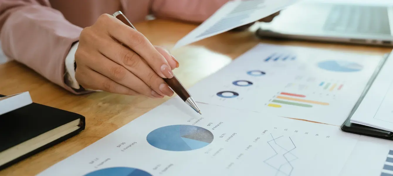 Mão a apontar para um gráfico circular em documentos de análise financeira