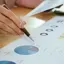 Mão a apontar para um gráfico circular em documentos de análise financeira