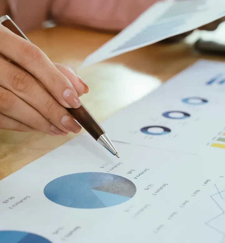 Mão a apontar para um gráfico circular em documentos de análise financeira