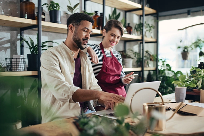 young couple consulting a computer placed on a countertop, surrounded by plants