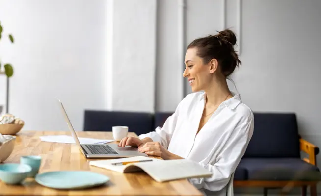Mulher sorridente a trabalhar no portátil numa mesa de madeira