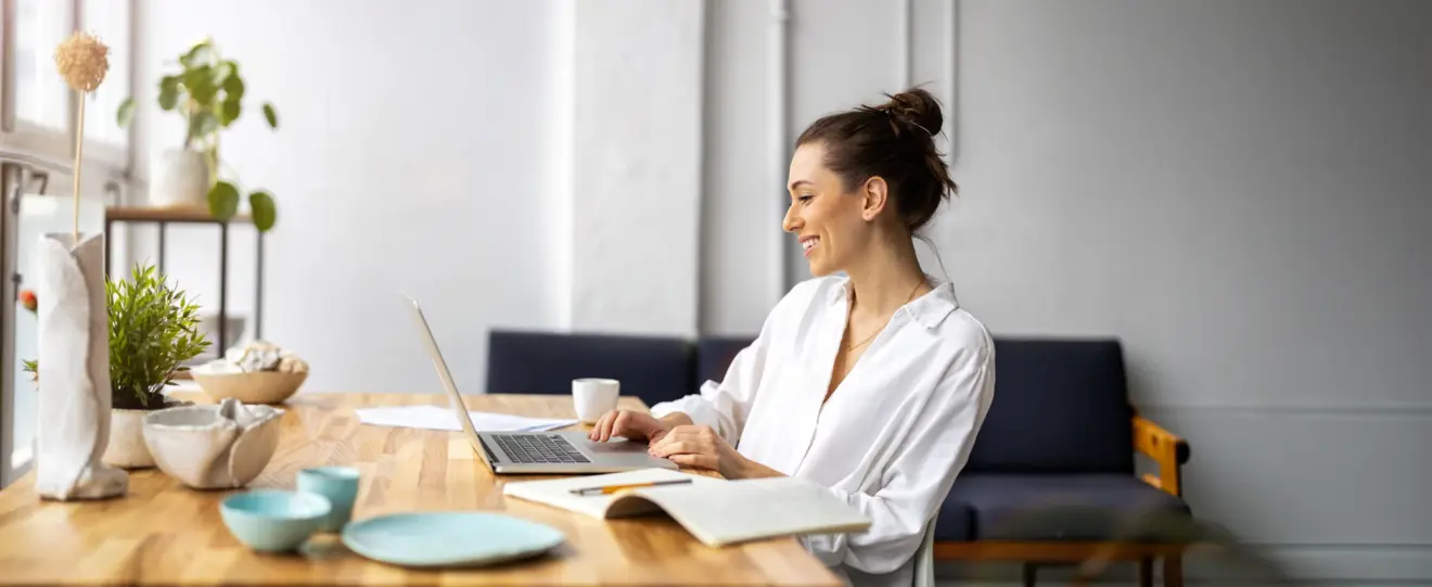 Mulher sorridente a trabalhar no portátil numa mesa de madeira