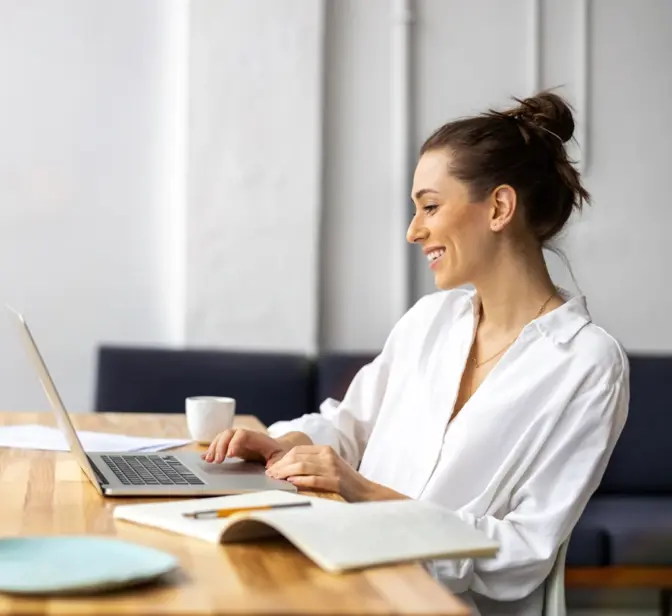Mulher sorridente a trabalhar no portátil numa mesa de madeira