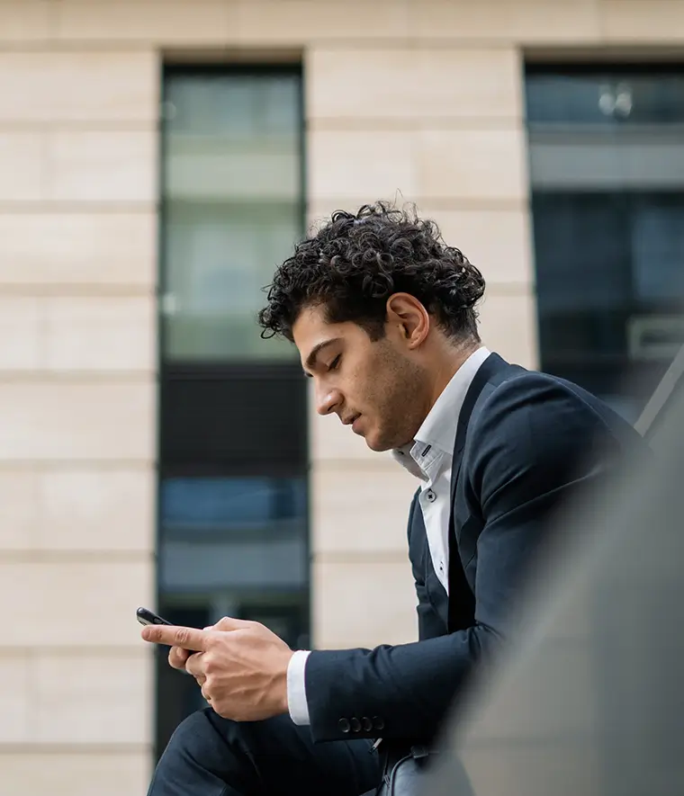 man in a suit, sitting on a bench outside the office, with a phone