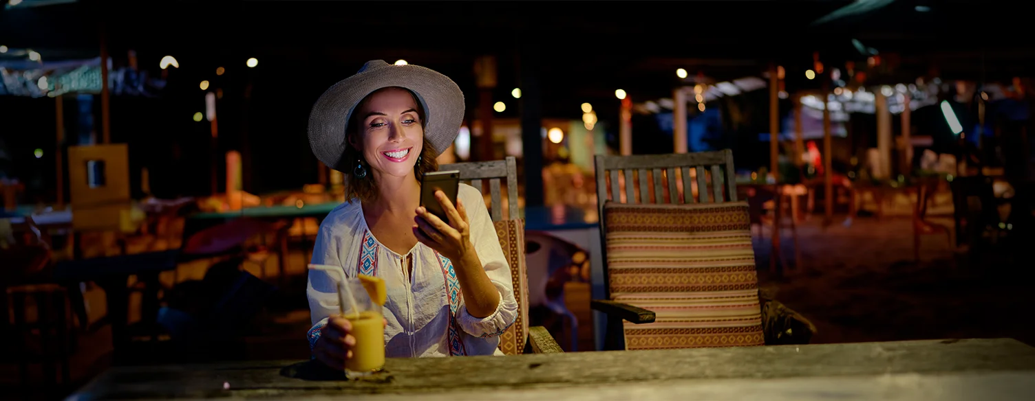 mulher sentada numa mesa de esplanada, à noite, a sorrir, com telemóvel na mão