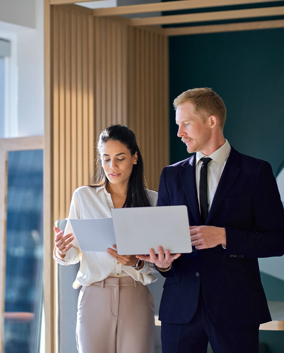 man and a woman in an office, holding a laptop and papers