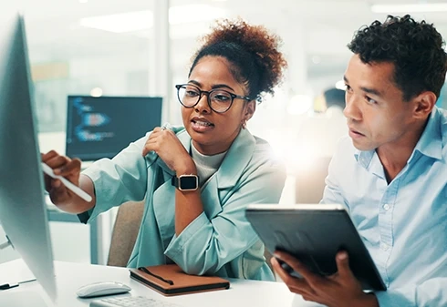 Dois colegas de trabalho a colaborar em frente a um ecrã de computador
