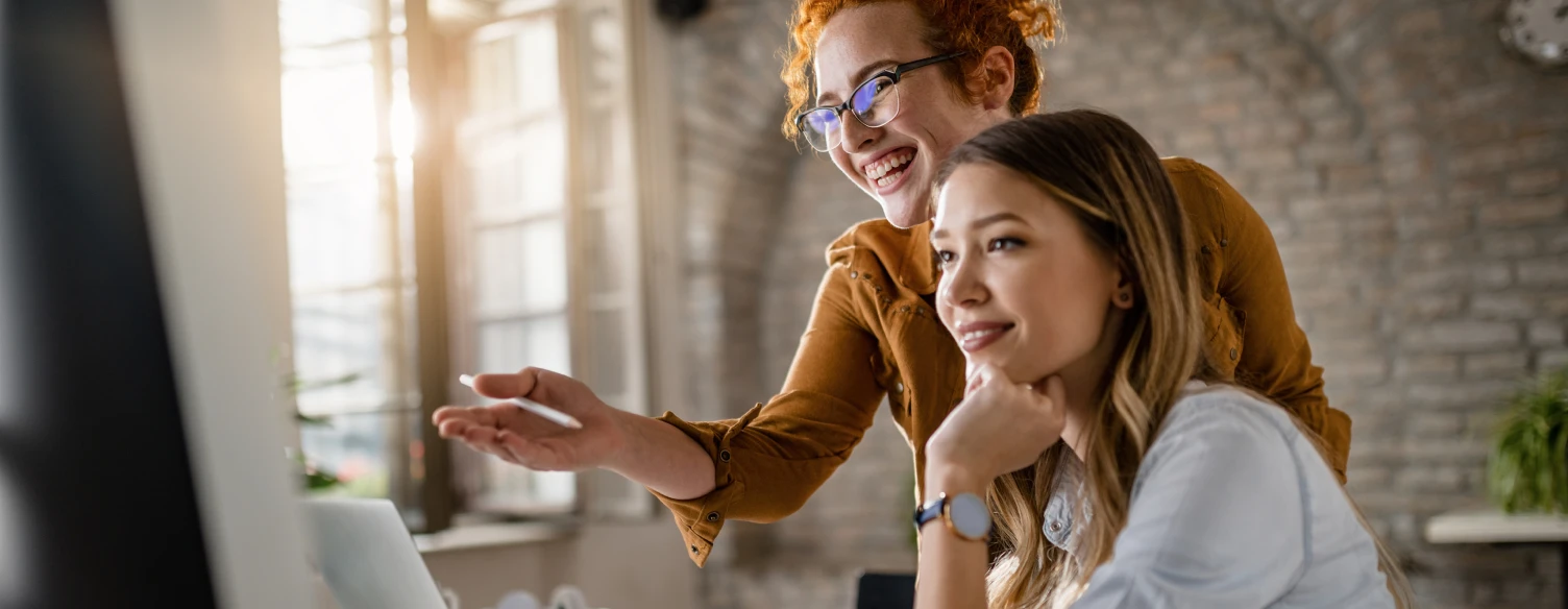 jovens empresárias felizes a colaborar enquanto utilizam o computador de secretária no escritório