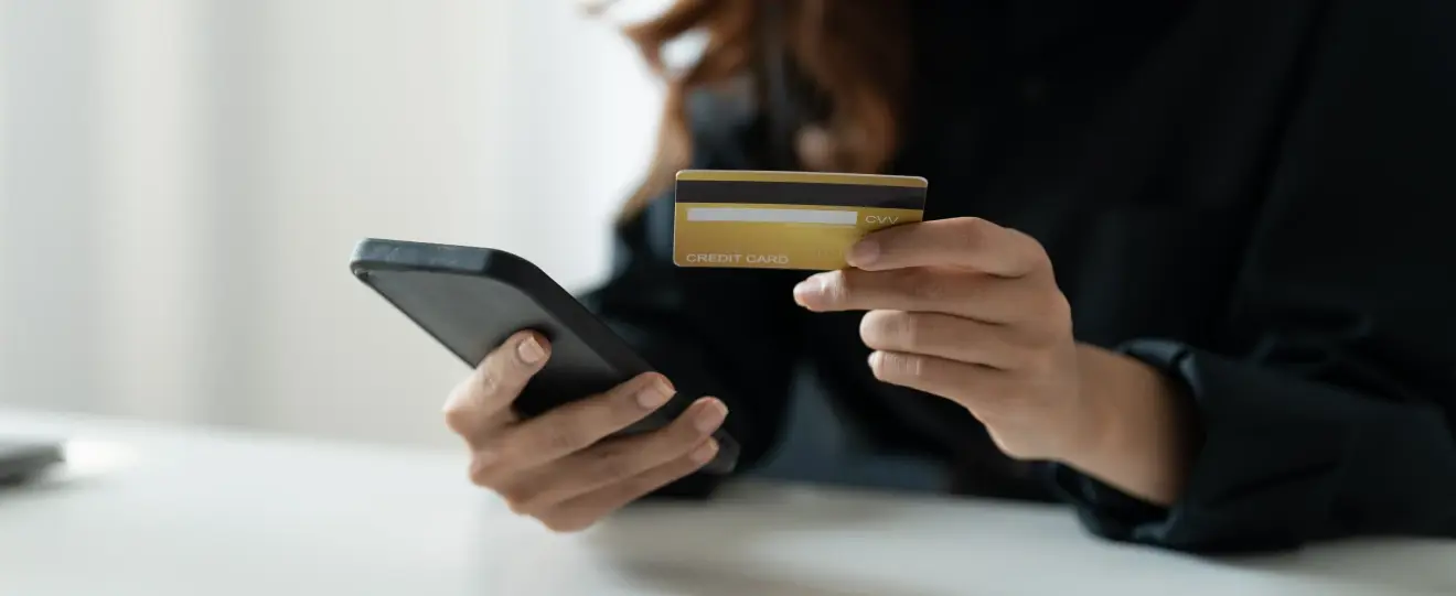 Mãos a segurar telemóvel e cartão de crédito dourado para pagamento online