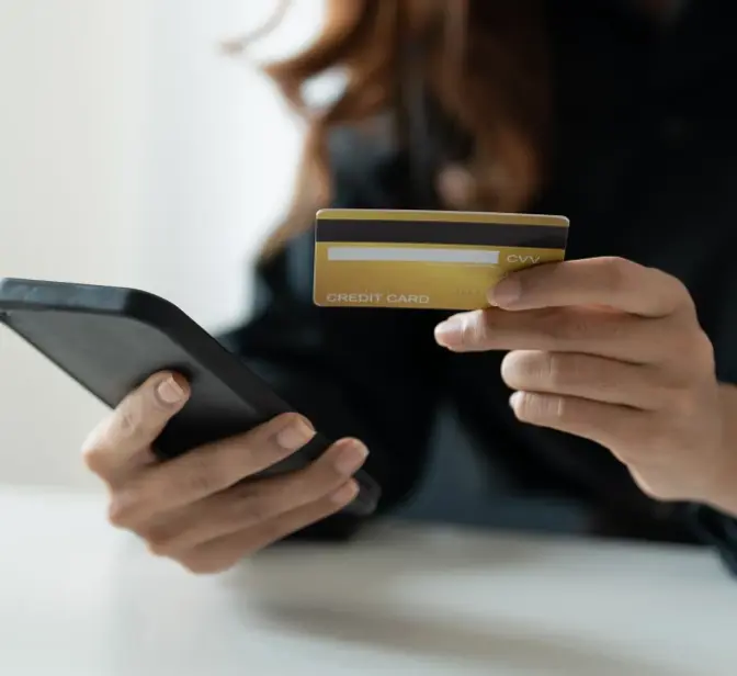 Mãos a segurar telemóvel e cartão de crédito dourado para pagamento online