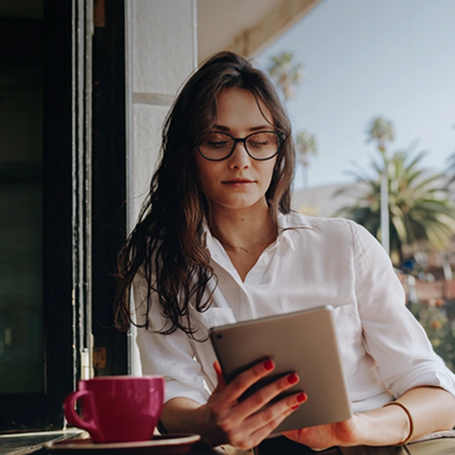 Woman using a tablet on a terrace with a coffee cup