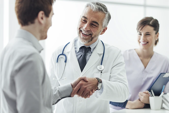 médico com estetoscópio ao pescoço, a dar aperto de mão a paciente