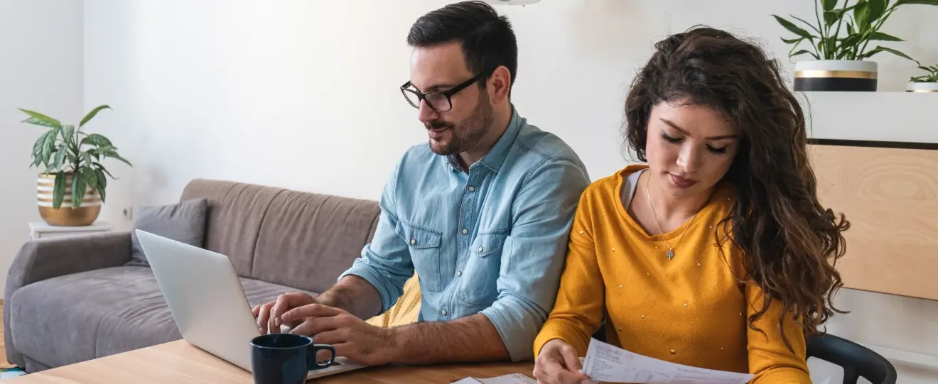 Casal sentado à mesa a planear finanças com um computador portátil e documentos