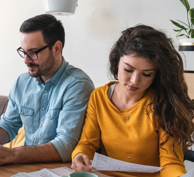 Casal sentado à mesa a planear finanças com um computador portátil e documentos