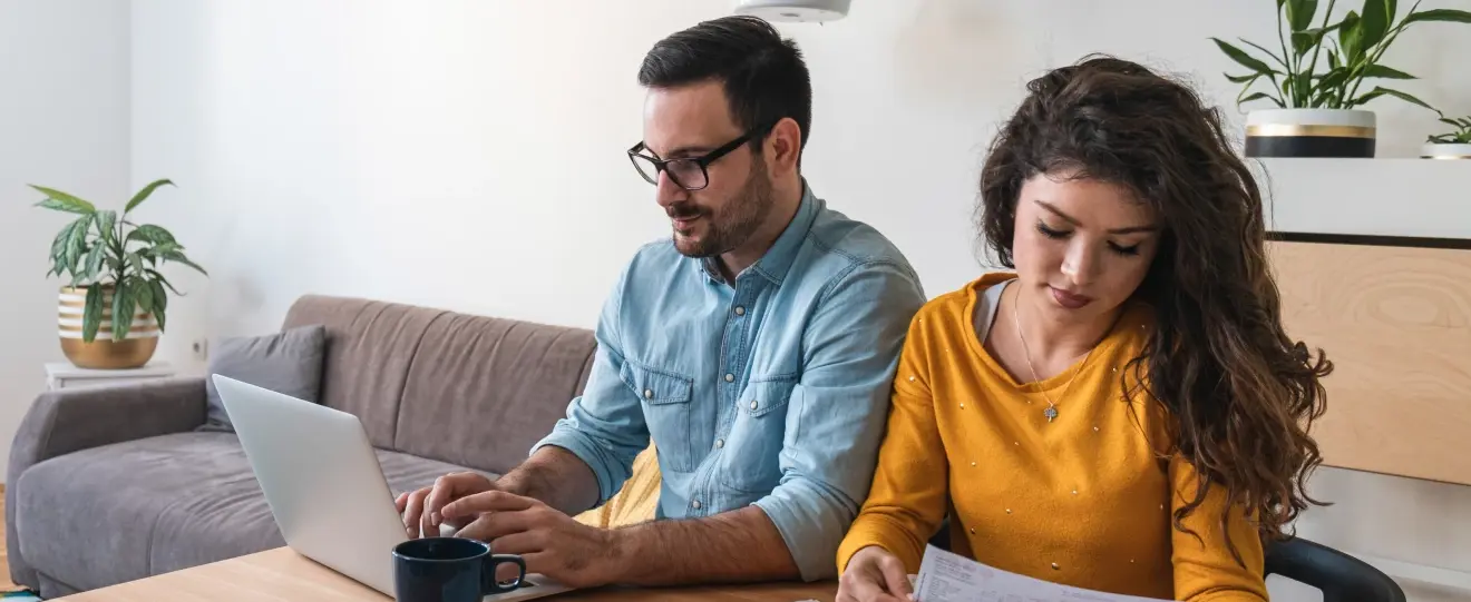 Casal sentado à mesa a planear finanças com um computador portátil e documentos
