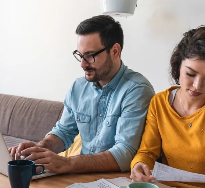 Casal sentado à mesa a planear finanças com um computador portátil e documentos
