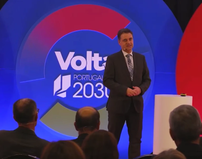 Homem, de fato e gravata com xadrez, a dar uma palestra