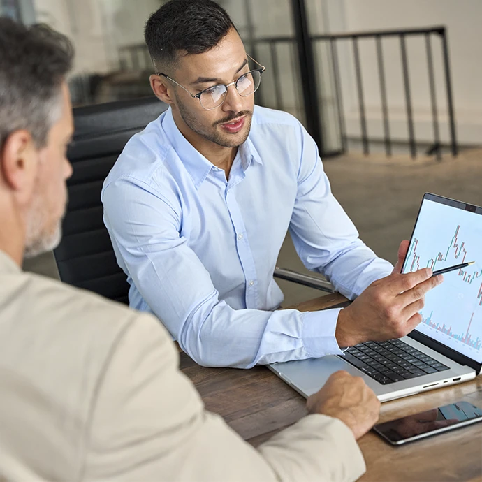 Rapaz a dar explicação no computador a colega sobre investimentos, no local de trabalho