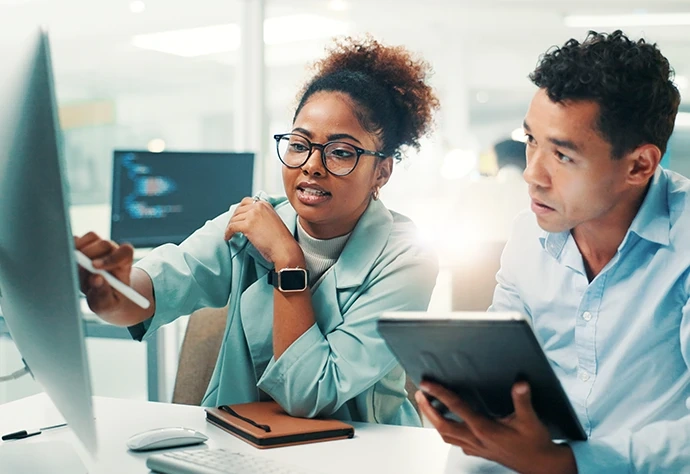 Dois colegas de trabalho a colaborar em frente a um ecrã de computador