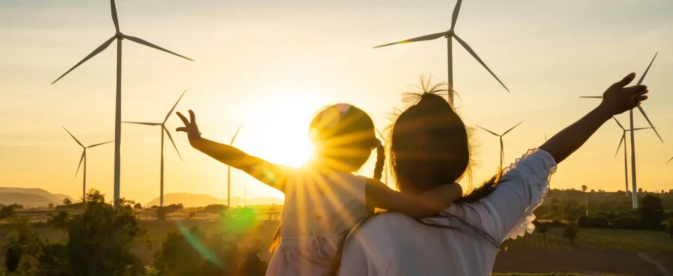 Mãe e filha olham para turbinas eólicas ao pôr do sol