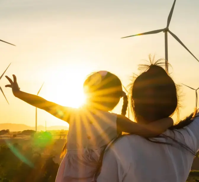 Mãe e filha olham para turbinas eólicas ao pôr do sol