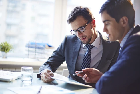 2 homens vestidos formalmente, numa reunião, com papéis