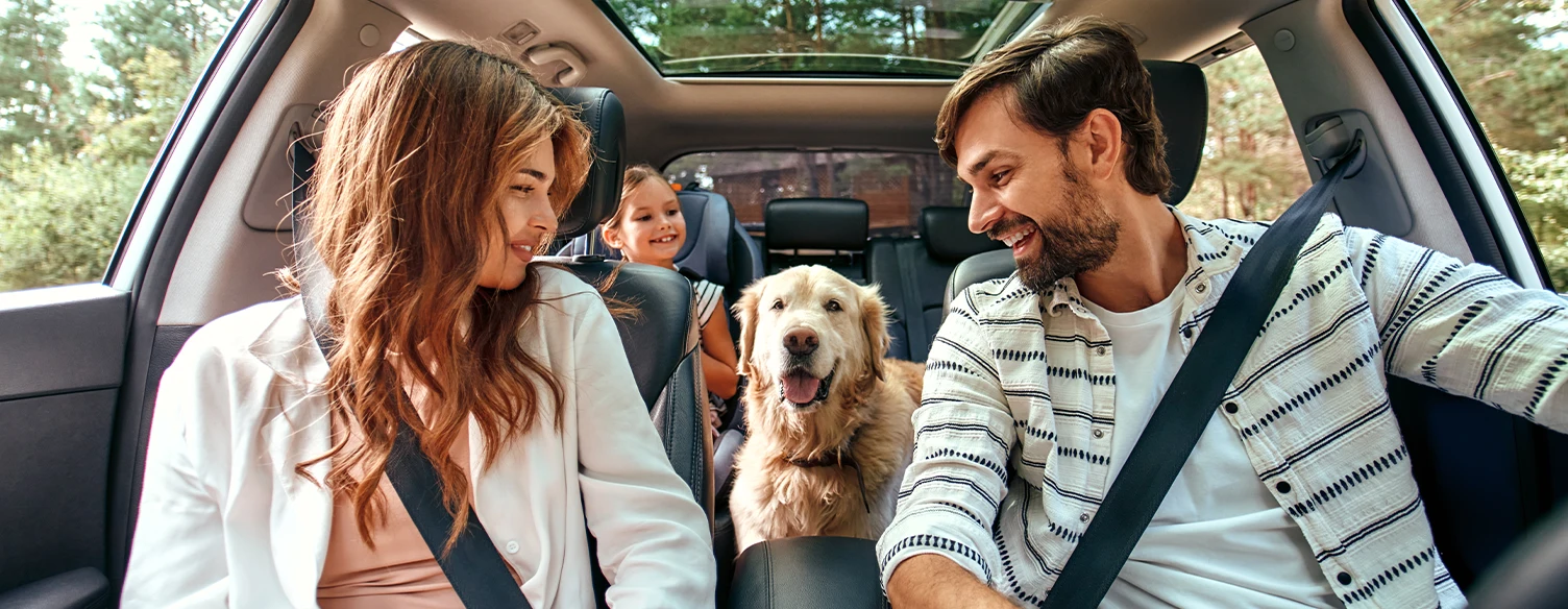 young couple with a daughter and a dog, inside their car, smiling