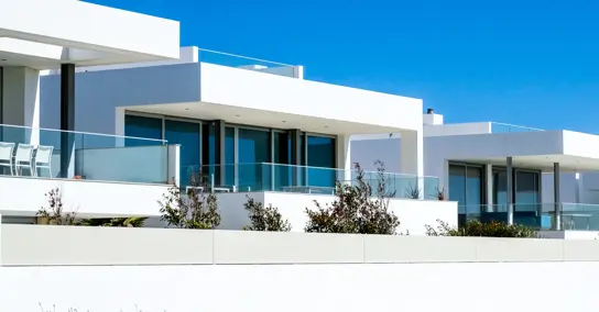 Casas modernas brancas com grandes janelas e varandas sob céu azul