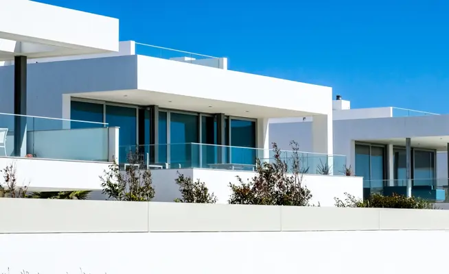 Casas modernas brancas com grandes janelas e varandas sob céu azul
