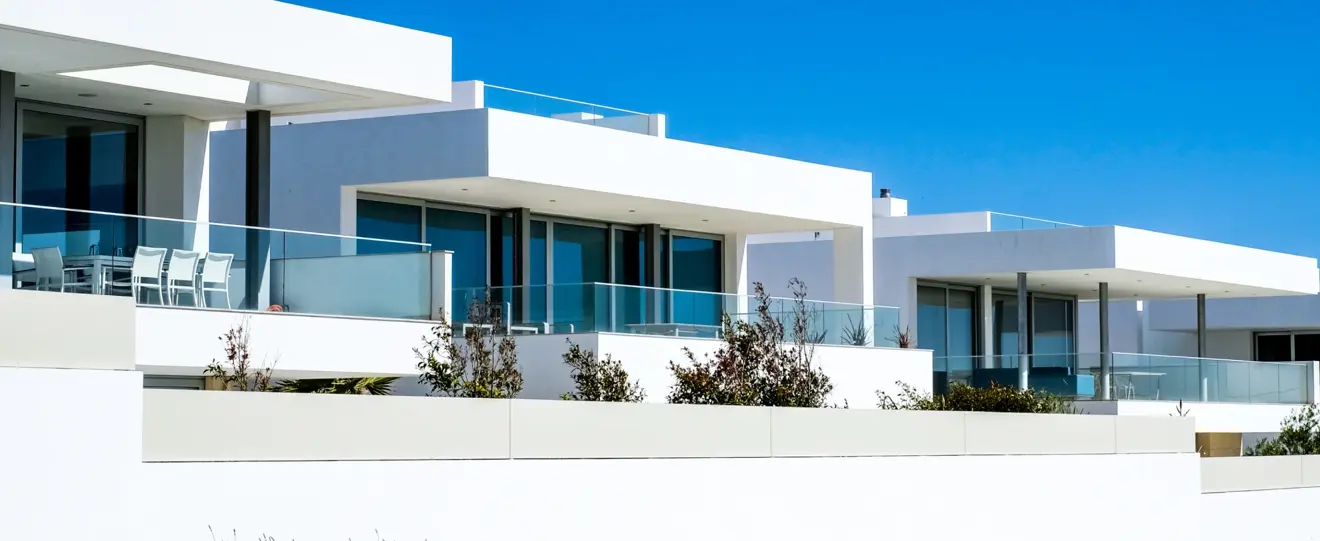 Casas modernas brancas com grandes janelas e varandas sob céu azul