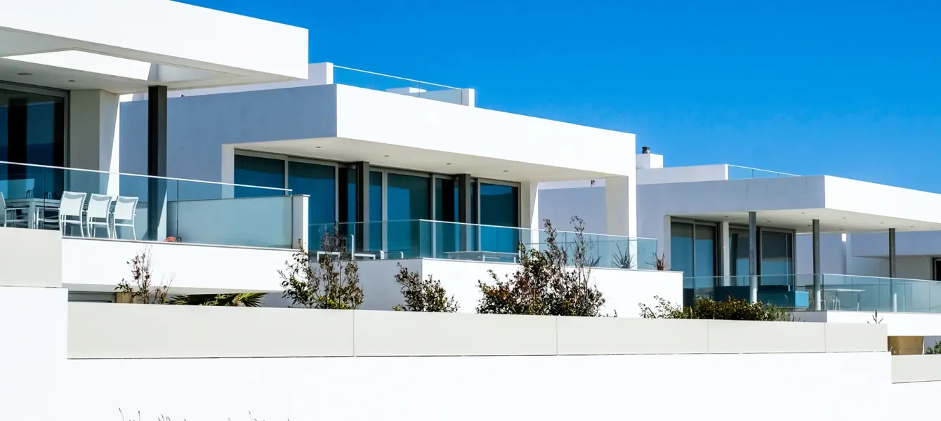 Casas modernas brancas com grandes janelas e varandas sob céu azul
