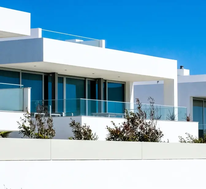 Casas modernas brancas com grandes janelas e varandas sob céu azul