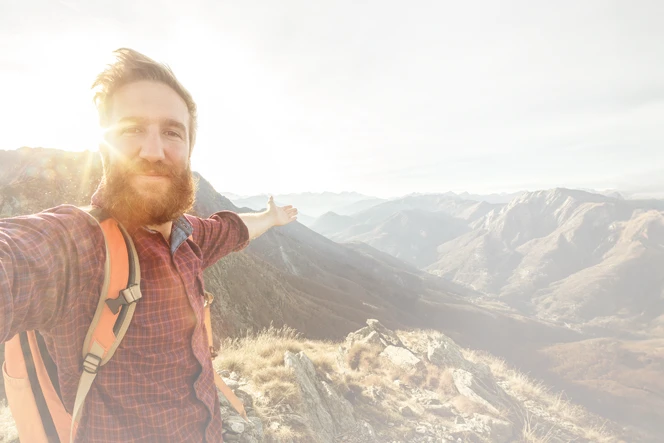 homem de barba, no topo de uma montanha, de braços abertos