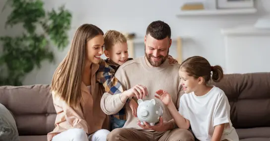 Família a colocar moedas num mealheiro cinzento no sofá