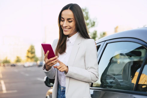 senhora com telemóvel, ao lado do seu carro