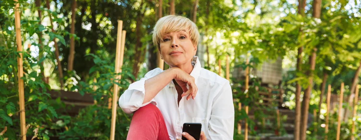 senhora sentada num jardim, com telemóvel na mão